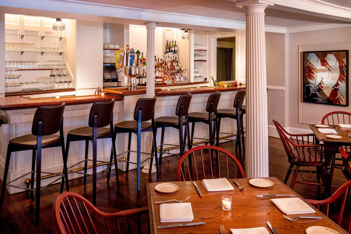 A stylish bar and dining space with a polished counter, comfortable bar stools, tasteful artwork, and intimate dining tables. The atmosphere is casual yet upscale, ideal for socializing, enjoying drinks, or savoring a meal with friends.